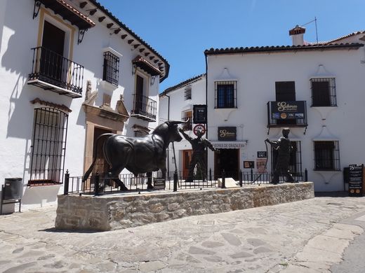 Monumento al toro de cuerda: un toro de bronce y dos hombres con la cuerda, ante casas blancas